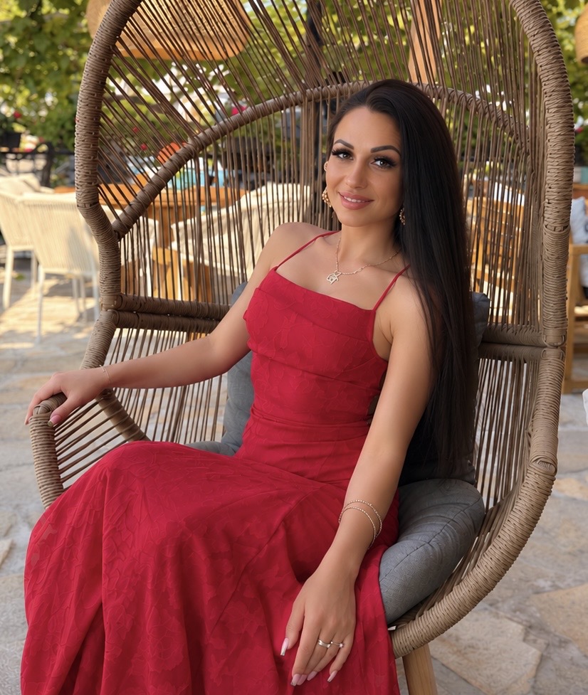 Mira — Avily character portrait in a red dress, seated in a rattan chair